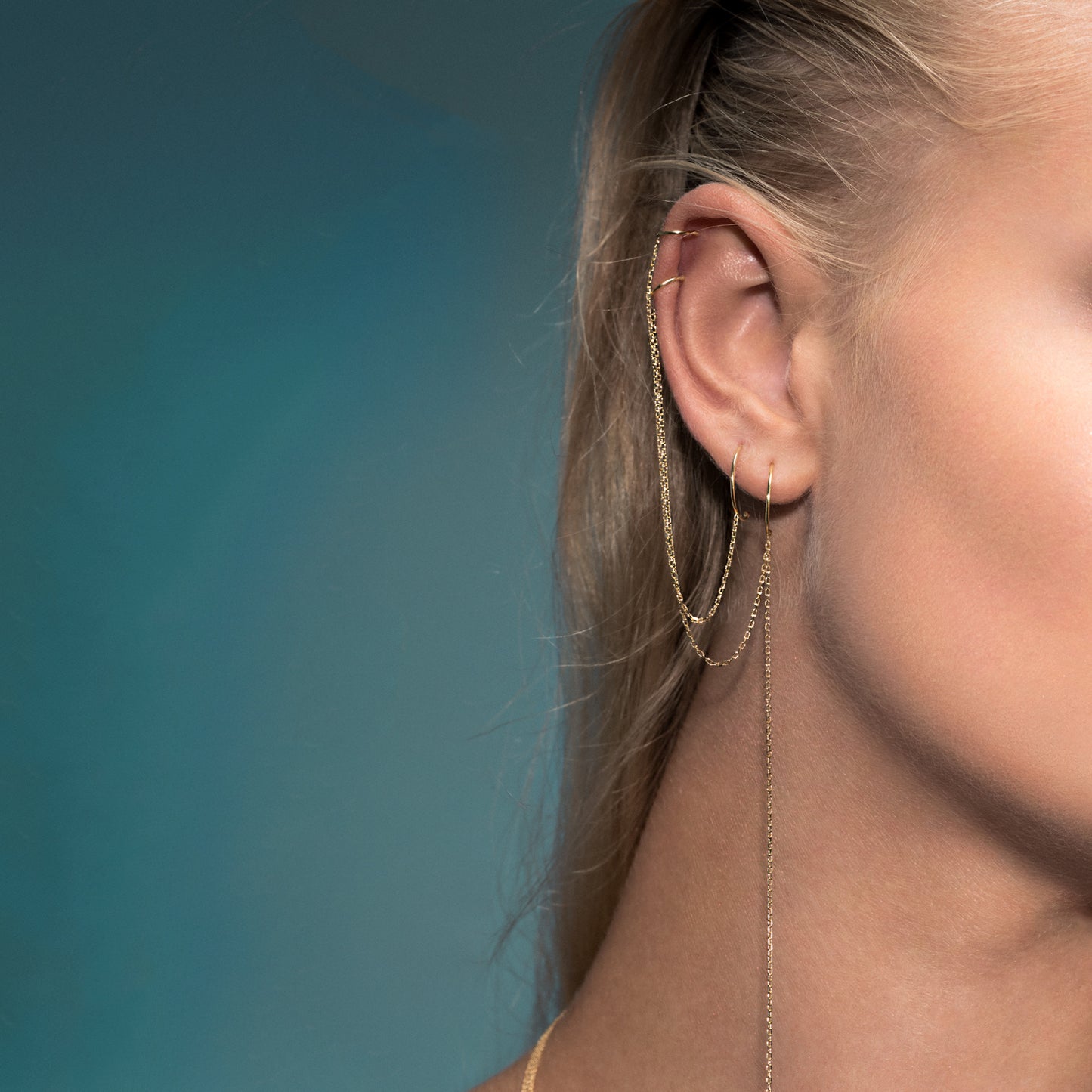 Model is wearing two Hoop to cuff earrings next to each other, the hoop to cuff with a dangling chain tail and the simple version that is a hoop connected to a cuff by chain.