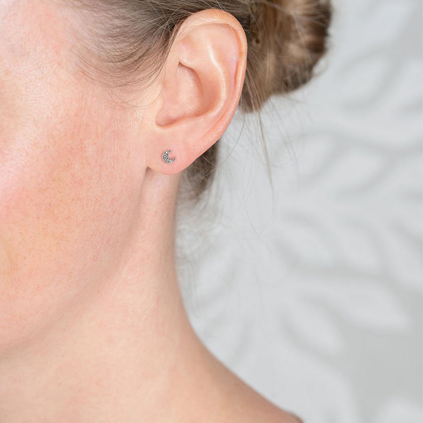 Laura Lee oxidised silver diamond set crescent moon stud earrings with 9ct yellow gold posts and butterfly backs seen on women's ear.