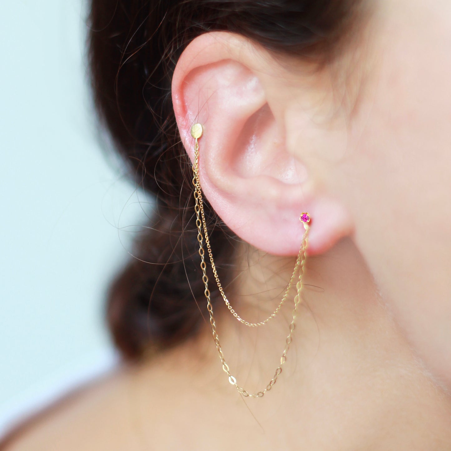 18ct yellow gold double stud earring with pink sapphire set collet and double connecting chain on model
