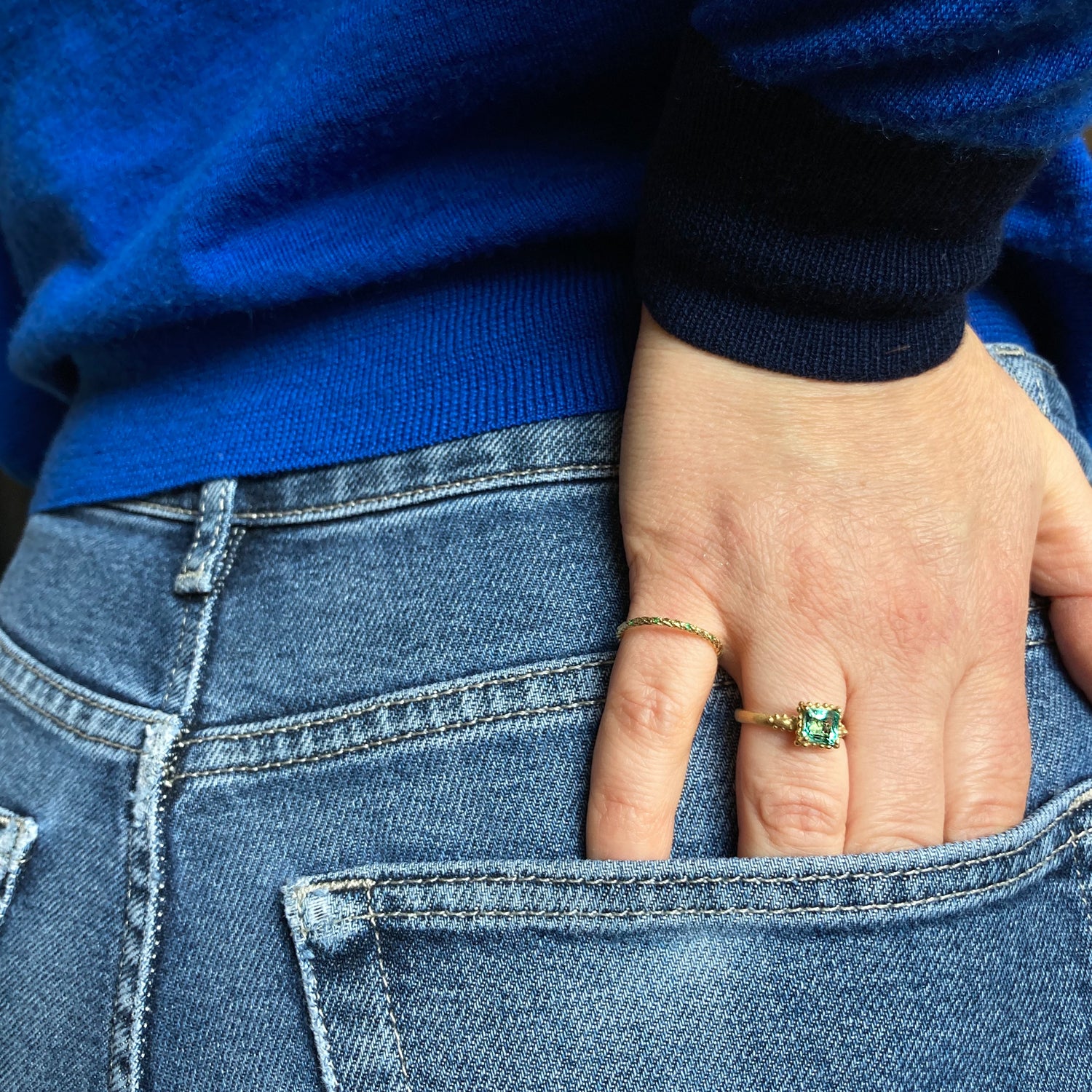 Ruth Tomlinson 18ct yellow gold ring with square facetted solitaire emerald with beaded granulation surround engagement ring on womens hand in pocket. Alternative engagement ring. Organic emerald ring.  